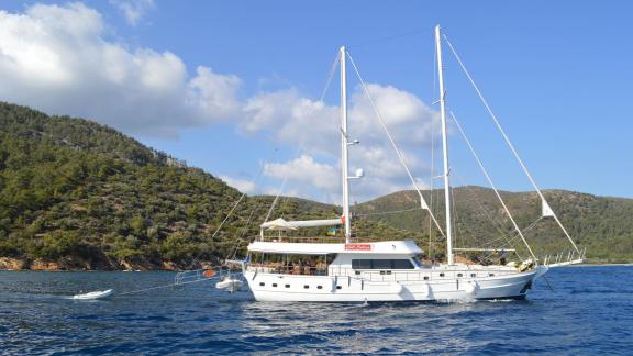 Der Gül Sultan Gulet ist vor der Küste von Bodrum vor Anker, mit grünen Bergen und blauem Wasser im Hintergrund.