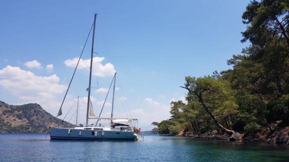 The Aldebaran sailing yacht is anchored in a peaceful bay, surrounded by green nature.