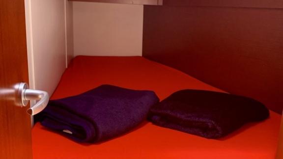 В каюте яхты Okhotnik есть двуспальная кровать с темным постельным бельем.