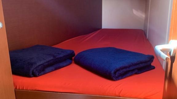 The cabin of the Okhotnik yacht features a double bed with a red cover and dark blankets.