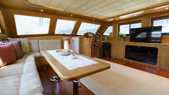 Spacious saloon of the Gulet Happy Hours with cosy seating area, large table and TV.