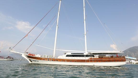 The gulet Holiday X with 10 cabins, anchored in Fethiye, features an elegant wooden construction and white sails.