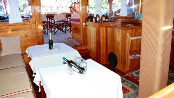 The interior of Gulet Il Fratello with a cozy salon, tables with wine bottles, and view of the aft deck.