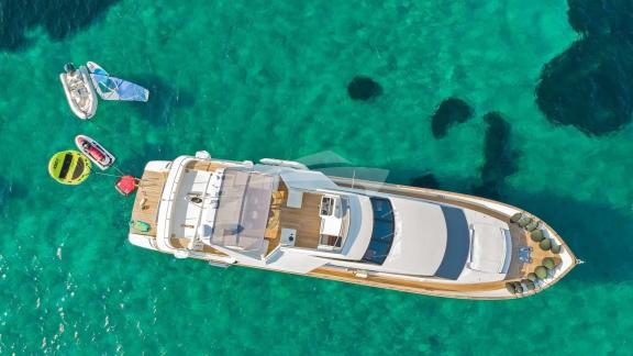 Die Illya F Yacht und verschiedene Wassersportgeräte im klaren Wasser von Mykonos von oben gesehen.