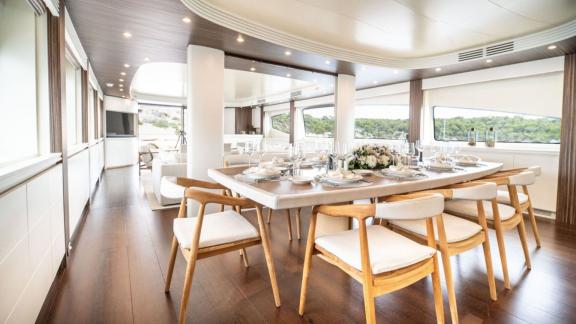 The dining area features a wooden table, elegant tableware and large windows with nature views.