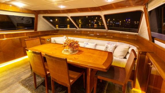 The main salon of Sveti Sky shows a wooden dining table and seating area under warm night lighting.