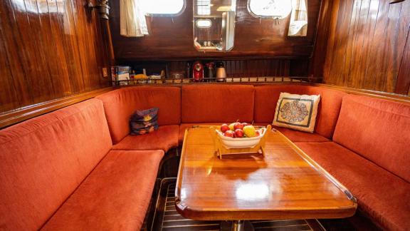 Interior view of the lounge with red sofas and wooden table on board Gulet Thalasa.