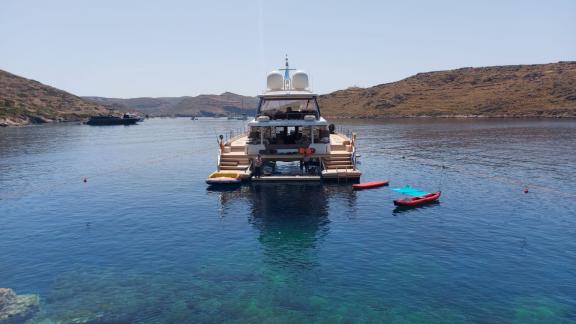 A luxurious catamaran is anchored in a serene, clear bay, with watersports equipment at the stern, available for charter