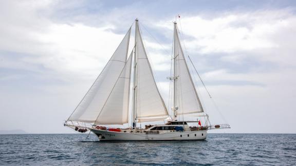 Die Gulet Kayhan 3 segelt mit vollen Segeln auf ruhigem Meer unter einem leicht bewölkten Himmel.