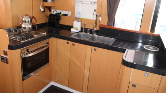 Wood-paneled kitchen in Catamaran Ayda1 with stove, oven, and double sink.