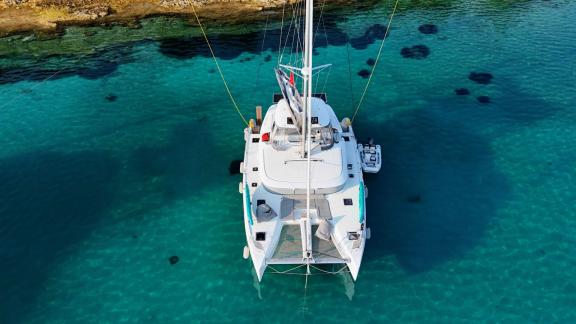 Zalina is anchored close to shore in shallow turquoise waters.