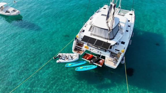 Die Zalina liegt vor Athen vor Anker, am Heckdeck sind Wasserspielzeuge, Paddleboards und ein Beiboot zu sehen.