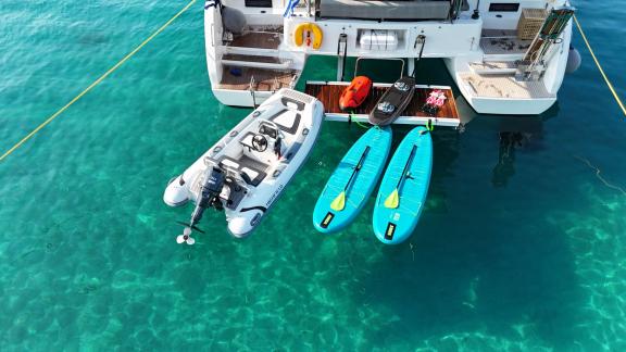 Der Katamaran Zalina liegt bei Athen vor Anker, mit Beiboot, Paddleboards und Wasserspielzeug auf der Badeplattform.