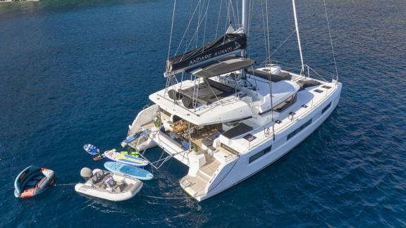 The catamaran is anchored off Athens, equipped with SUPs, tender boats, and water gear.