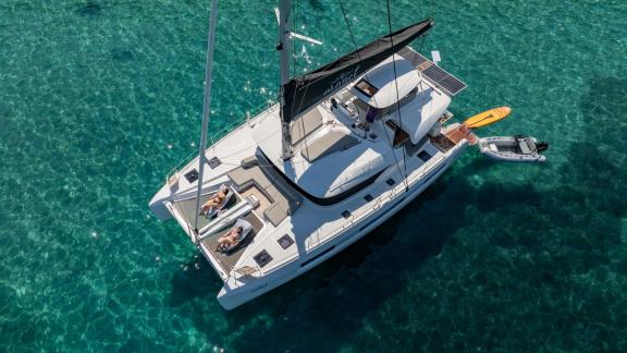 Aranel is anchored in turquoise water, guests sunbathe on foredeck, tender alongside.
