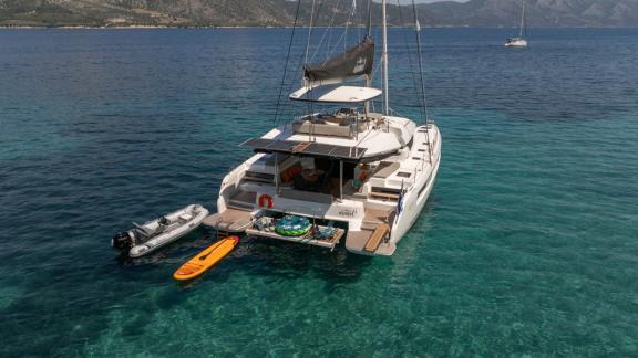 Aranel is anchored in a turquoise bay, paddle board and tender tied at stern.