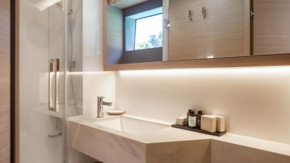 The bathroom of Aranel catamaran in Lefkada features a sink, mirrored cabinet and glass shower.
