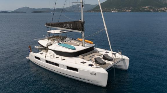 Aranel is anchored in calm sea, with cushioned foredeck and shaded flybridge lounge.