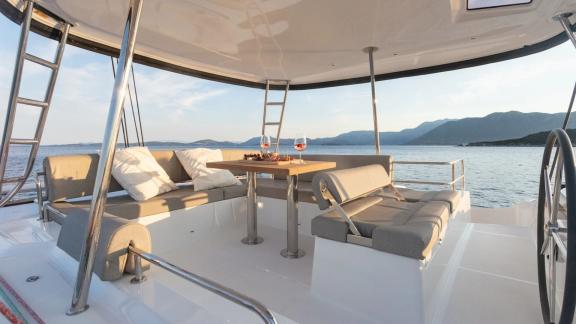The flybridge of Aranel catamaran in Lefkada features lounge seating and a table with sea views.