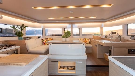 The saloon of Aranel catamaran in Lefkada features a U shaped sofa, galley and panoramic windows.