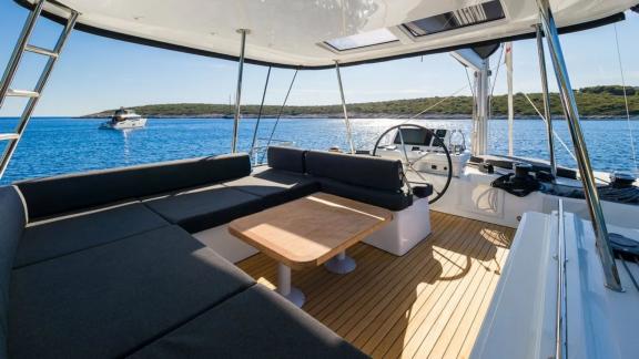 На флайбридже катамарана Lagoon 51 Catwalk расположены штурвал, диваны и стол с видом.