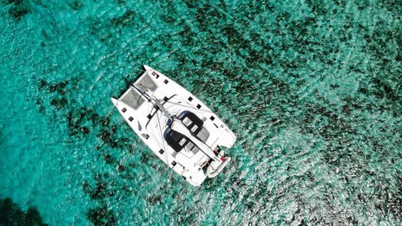 Akana floats in crystal-clear water, captured by drone from directly overhead.