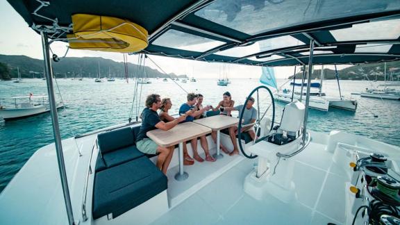 A group relaxes around the table on Akana with anchored boats in the background.