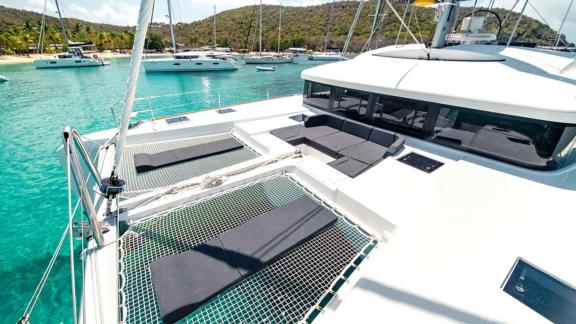 Akana is anchored with sun pads on netted deck and a clear bay in the background.