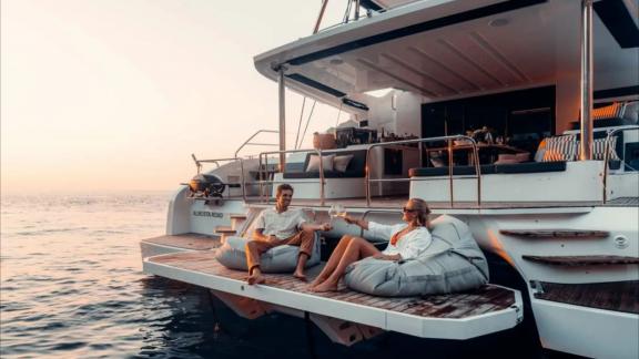 Two guests relax with drinks at the water’s edge during a peaceful sunset.