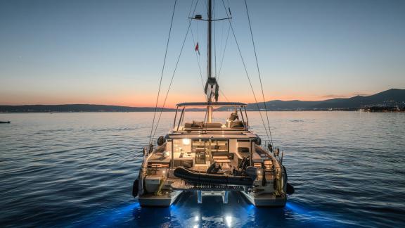 The Lagoon 55 Tri Wing glows from the stern with underwater lights as the sun sets over Kastela bay.