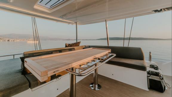 The Lagoon 55 Tri Wing features a cushioned dining area with wooden table and sea view in Kastela.