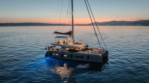 Among catamaran rental options in Kastela Triwing Ossus is seen anchored in calm sea during sunset.