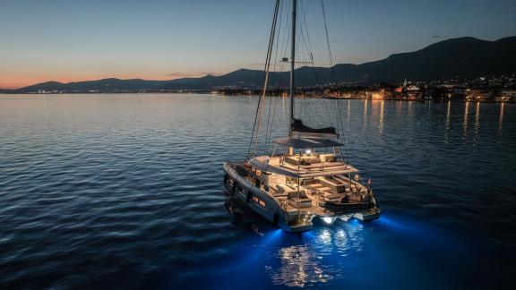 Among catamaran rental options in Kastela Triwing Ossus is seen illuminated at night anchored in calm sea.