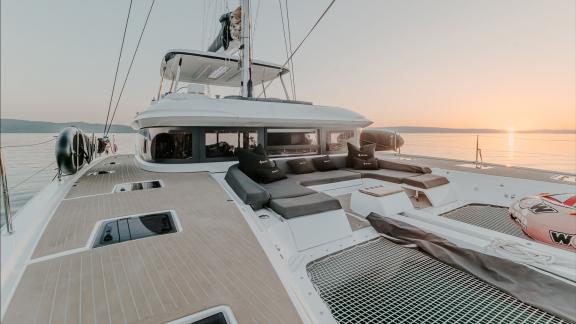 Among catamaran rental options Triwing Ossus front deck seating area is seen anchored in calm sea during sunset.