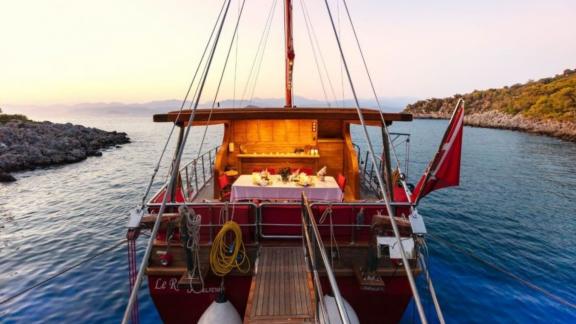 Yacht with an elegant dining table on the deck, surrounded by calm sea at sunset.