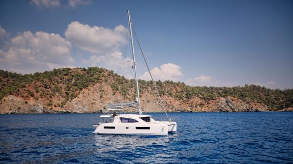 The catamaran Derya sails peacefully in a picturesque bay with a mountain backdrop.