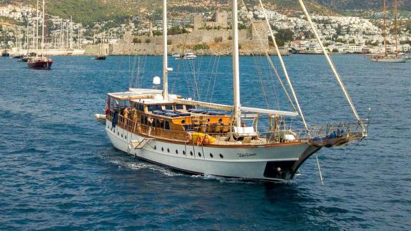 A traditional Turkish gulet sails off the coast of Bodrum, Turkey. Bodrum Castle and the town are visible in the backgro