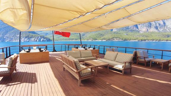 Enjoy relaxed seating on the spacious yacht deck with a view of the coastline and blue waters.