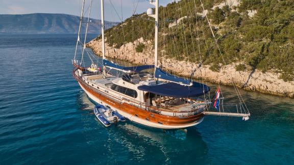 The gulet Lotus is anchored in a picturesque bay in Croatia, surrounded by clear blue water and rocky coasts.