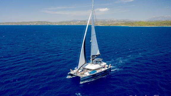 The Catamaran Lucky Clover sails majestically in front of a stunning coastal landscape.