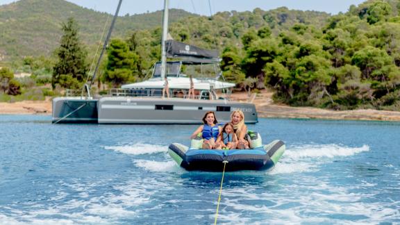 A family enjoys thrilling water sports behind Catamaran Lucky Clover in a scenic bay.