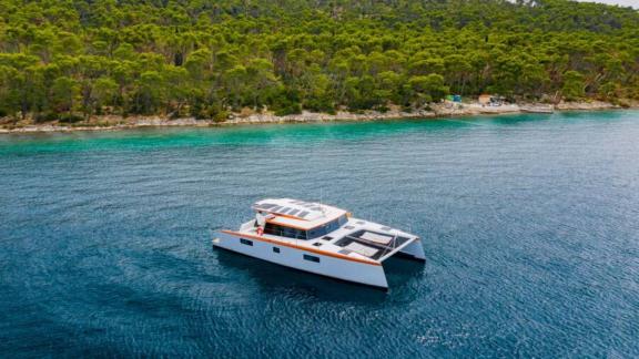 В Сплите катамаран Orange стоит у берега с лесом и сеткой на носовой палубе.