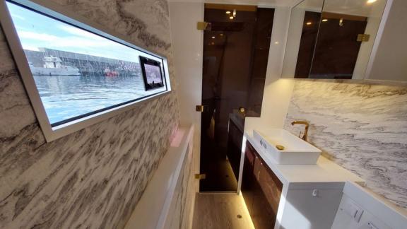 The bathroom features marble walls, a window, gold faucet, rectangular sink and mirrored cabinet.