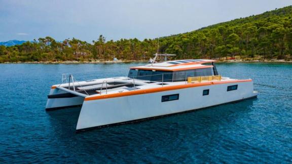 В Сплите катамаран Orange стоит в бухте с сеткой на носу и диваном у кормы.