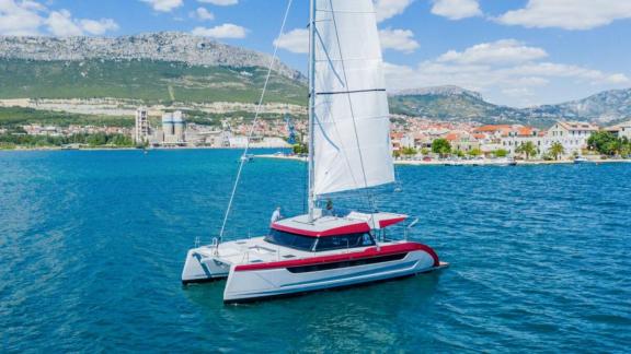 Kırmızı-beyaz Luna 49 Red katamaran, Split şehir manzarası önünde yelken açmış şekilde Adriyatik'te seyrediyor.