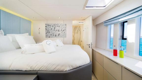 The master cabin of Sunreef 50 Solitaire features a large bed, en-suite bathroom, and wide windows facing the sea.
