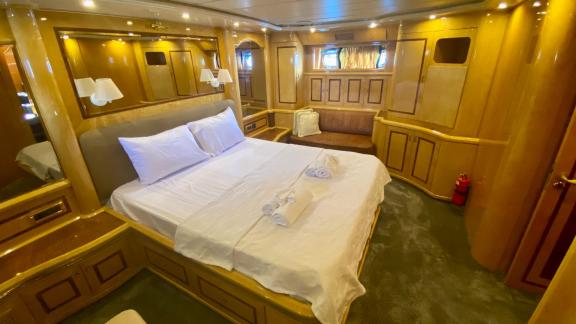 Spacious cabin of motor yacht Ser 1 featuring a large bed, seating area, and wooden details.