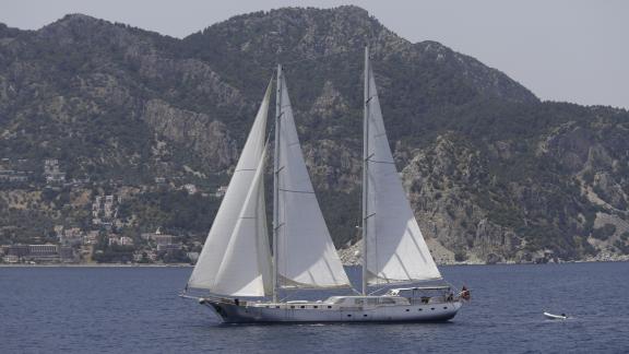 The Silver Moon sails calmly in front of a stunning mountain backdrop.