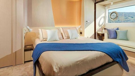 Helle Kabine mit großem Bett, Sofaecke und Fenster mit Meerblick.