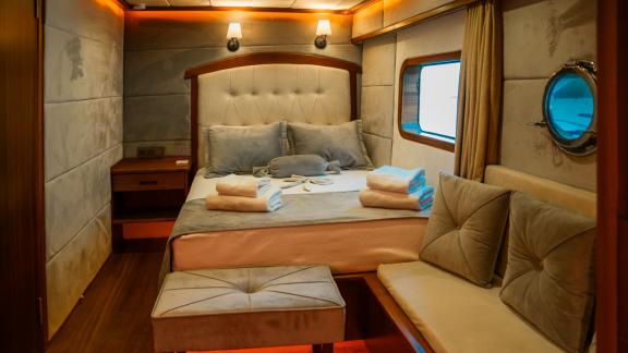 Comfortable guest cabin with soft lighting, seating area, and porthole aboard the Oggusto.